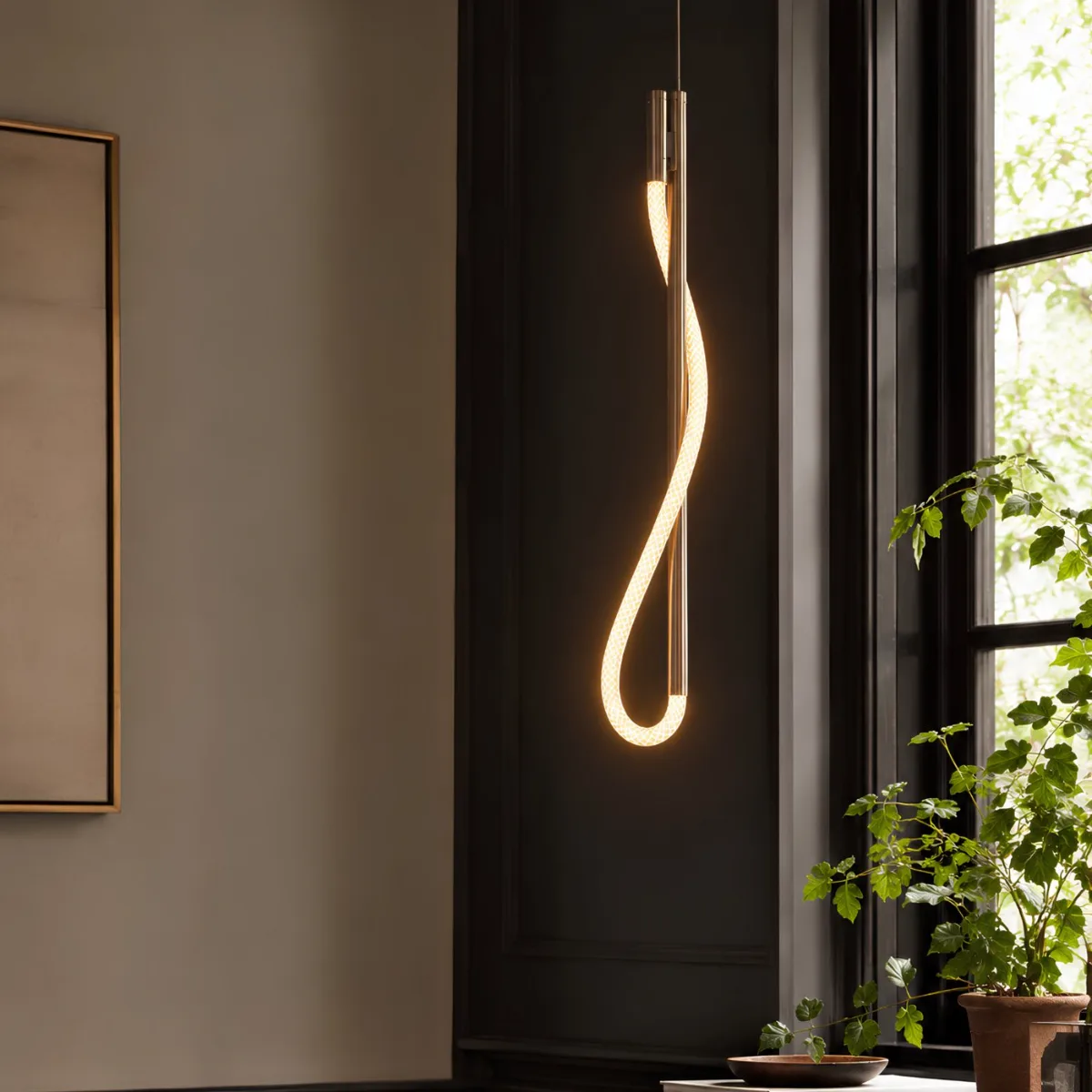 Eden pendant in polished nickel — a single illuminated cord looped around a slim vertical stem, against dark paneling beside a window