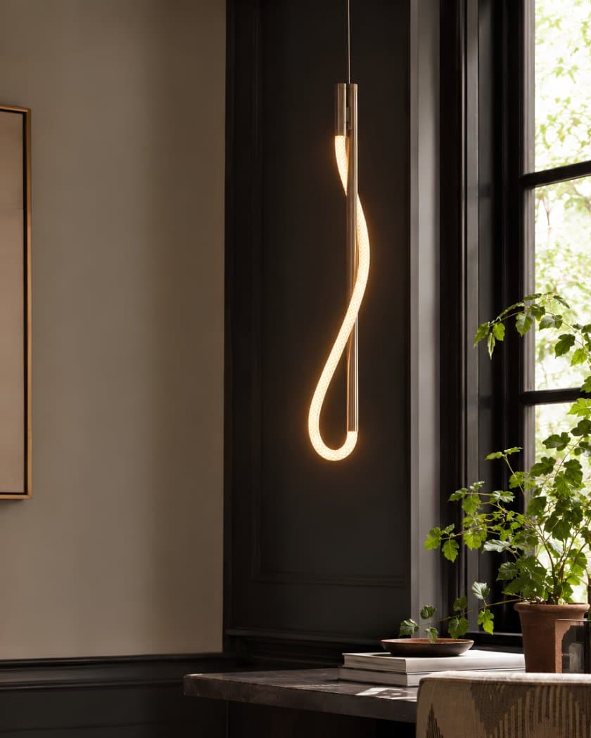 Eden sculptural suspension in satin brass — illuminated cord drawn through open metalwork in a quiet corner vignette