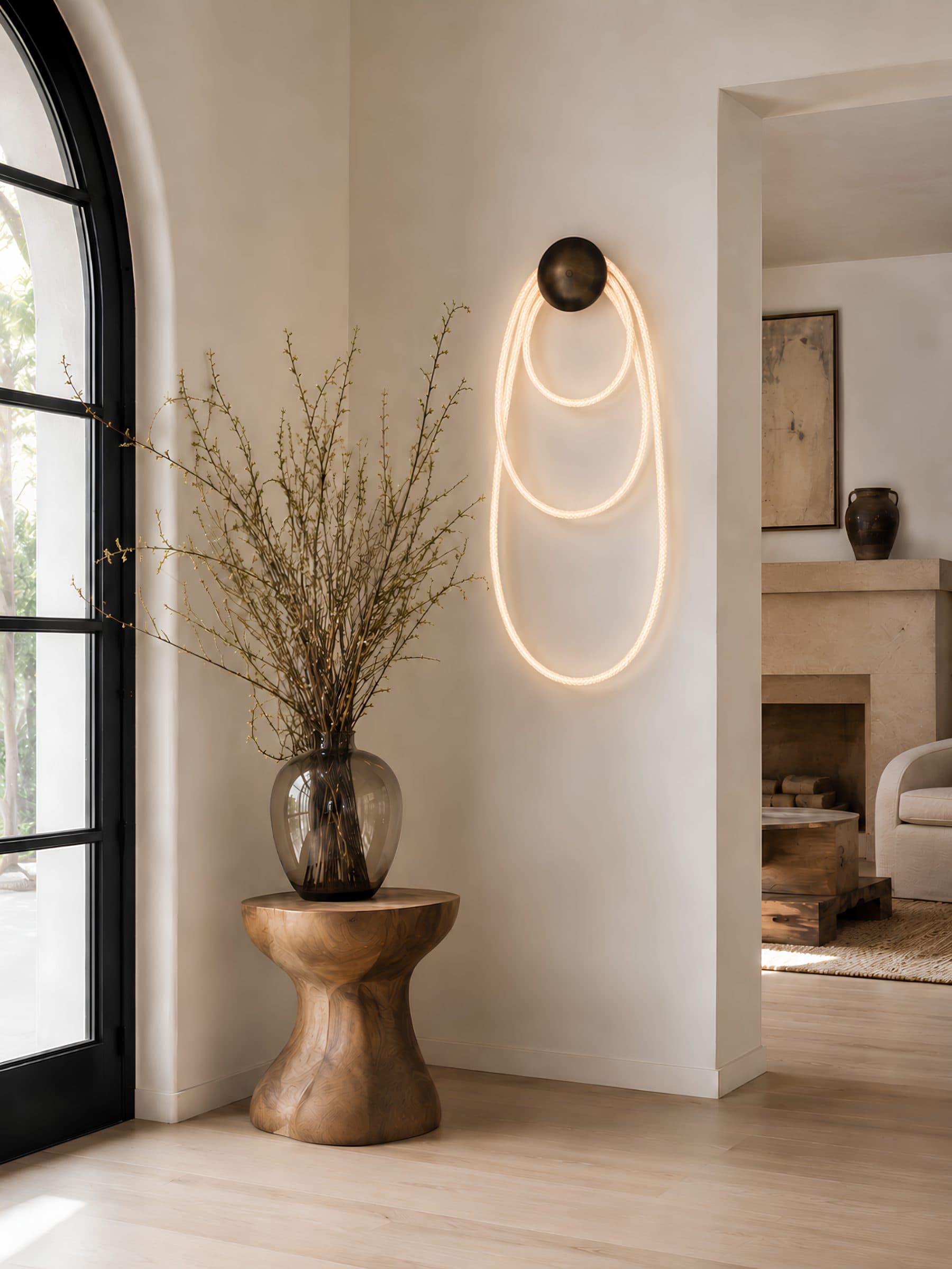 Selene I in blackened brass on a plaster wall beside an arched window — illuminated cord looped in three nested ovals from a single dome canopy