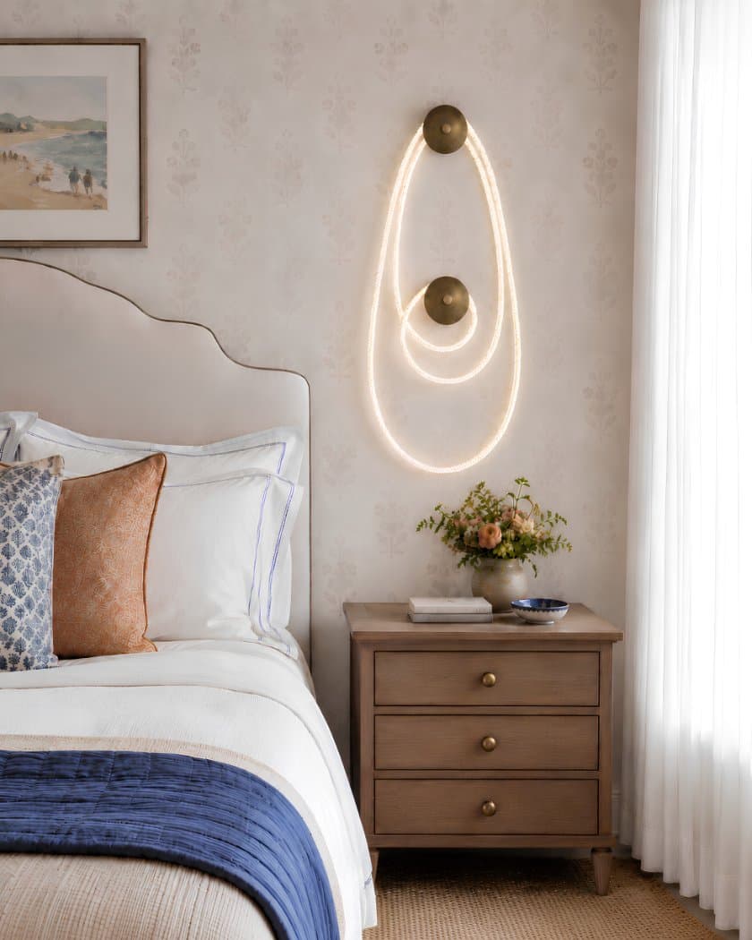 Selene II in aged brass above a bedside table — illuminated cord looped around two dome canopies