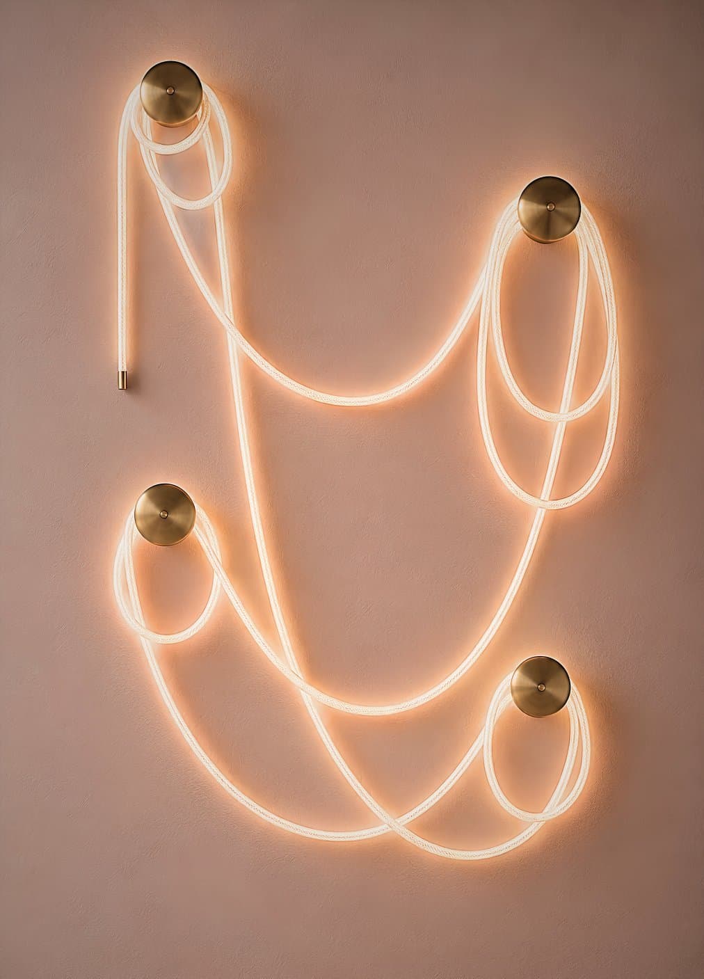 Selene Traverse composition — illuminated braided cord looped between four brass wall canopies on a warm plaster wall