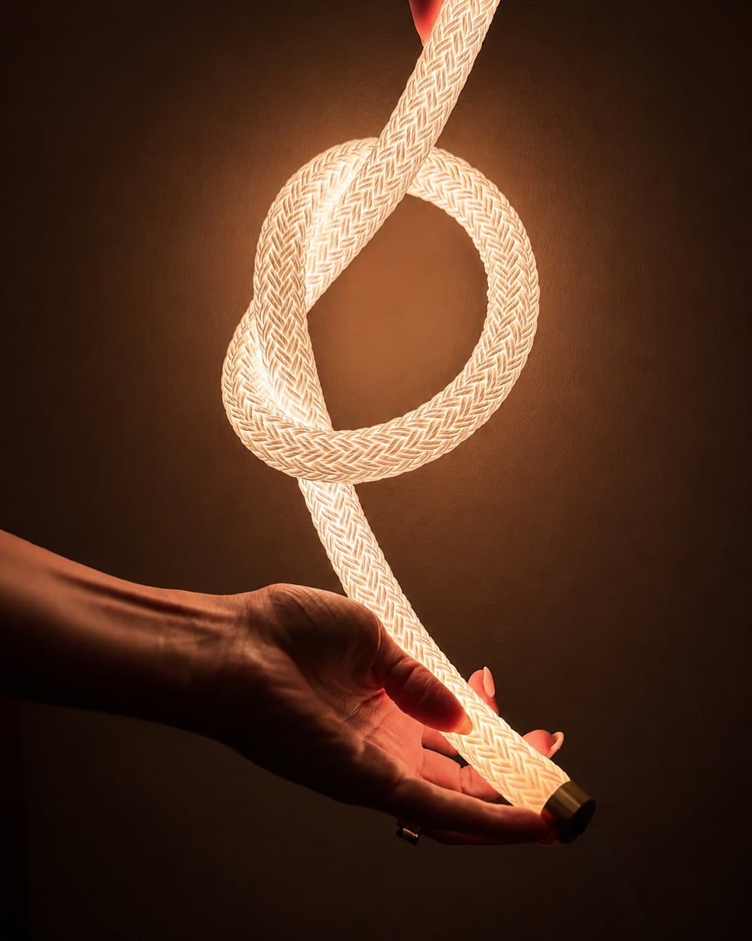 Hands holding a knotted length of illuminated braided cord with a brass end cap